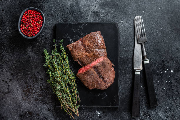 istock Grilled Top Blade or flat iron roast beef meat steaks on marble board. Black background. Top View 1313013524