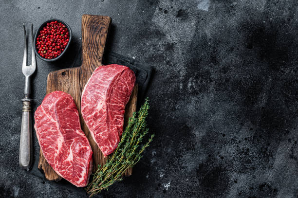 istock Fresh Raw Top Blade or flat iron beef meat steaks on a butcher cutting board. Black background. Top View. Copy space 1313013624