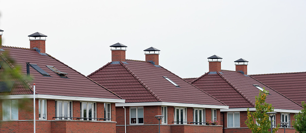 Summer evening close-up of rooftops in a new Dutch residential area with semi-detached red brick houses having red tiled, pointy roofs, skylights and chimneys