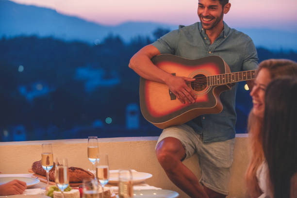 istock Group of friends having a dinner party with one man playing guitar. 1313020581