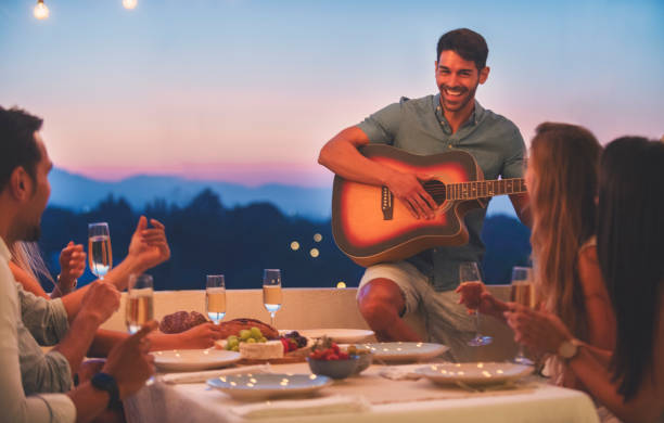 istock Group of friends having a dinner party with one man playing guitar. 1313020583