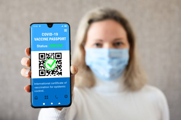 Woman holds smartphone with COVID-19 vaccination passport COVID-19 vaccination passport in mobile phone for travel, woman wearing mask holds smartphone with health certificate app, digital coronavirus pass. Concept of corona virus and immunity passport. (Fake screen of phone) vaccine passport photos stock pictures, royalty-free photos & images