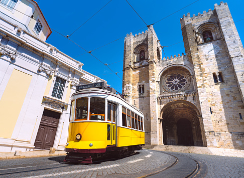 Lisbon city old town and famous yellow tram 28 in front of Santa Maria cathedral on a sunny summer day. Trams in Lisbon, Portugal. Tourist attraction. High quality photo