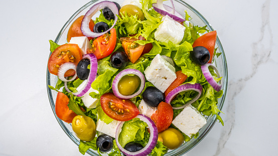 Top down view of bowl with Greek salad. Mixture of fresh vegetable, olives and feta cheese. Raw food and healthy lifestyle concept.