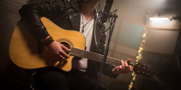 istock Midsection of man playing acoustic guitar. Man sitting at studio microphone. 1313030697