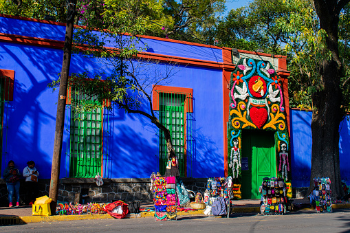 Mexico City, Mexico - January 13, 2021: Street vendors on sidewalk outside the museum of famous Mexican painter. Blue and red building with beautiful arch over the entrance. Museums from Mexico