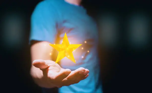 Photo of Man in a navy blue shirt holding a golden star sparkling against a black backdrop. Being a winner Concept. Being the best Concept.