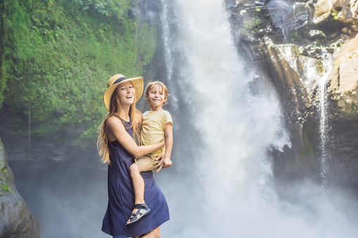 Mom and son tourists on the background of a waterfall. Traveling with kids concept. What to do with children Children friendly place.