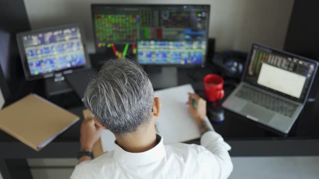 high angle view asian matured chinese man with gray hair working at home with stock exchange market multiple computer monitor monitoring market trend