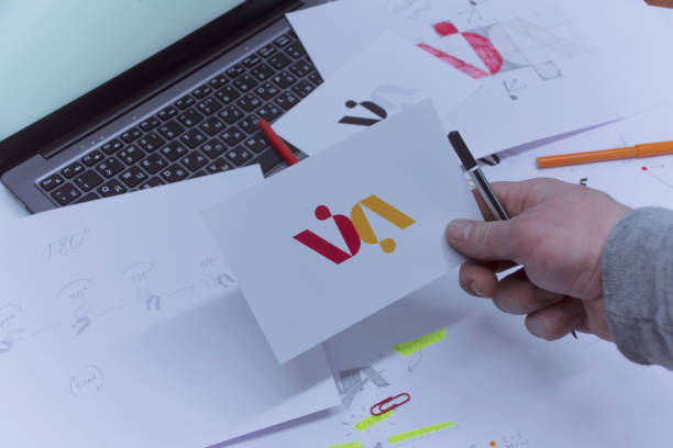 Creative workplace of a Graphic Designer. A man in the office is developing a logo on the table against the background of printed sketches and a laptop.
