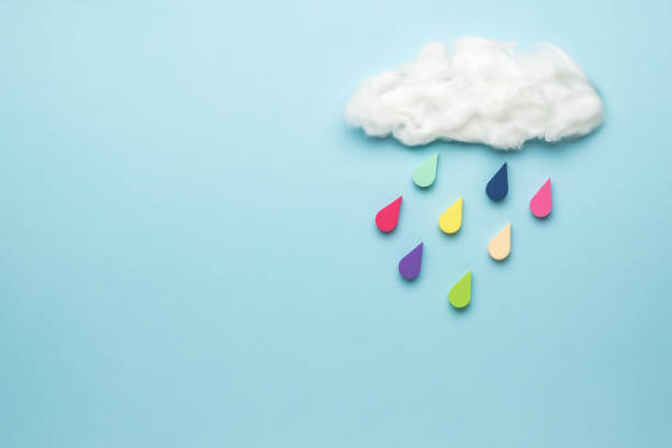 istock Multicolored drops fall from a cloud on a blue background. Climate picture. 1313058637