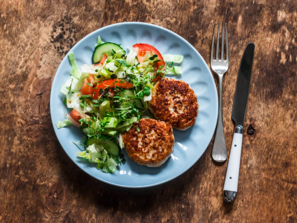 turkey burgers and fresh iceberg, tomatoes, cucumber salad on a wooden background, top view. balanced lunch - turkey burger imagens e fotografias de stock