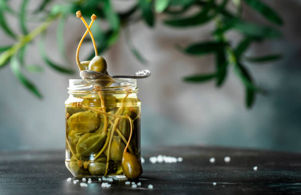 istock Capers. Marinated or pickled canned capers fruit close up in glass jar on gray kitchen table background. Copy space 1313067660