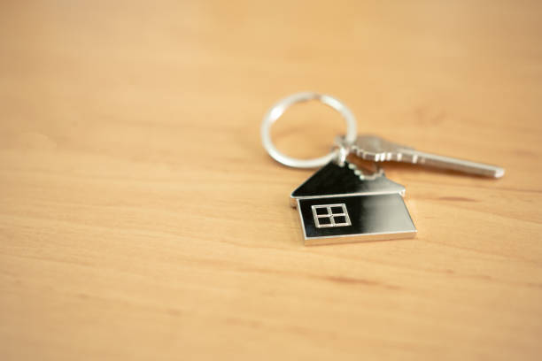 istock Selective focus at the home shape iron key chain with the key that put on wood table surface inside of the house. Home ownership, mortgage or property loan finance concept with copy space for text. 1313069515