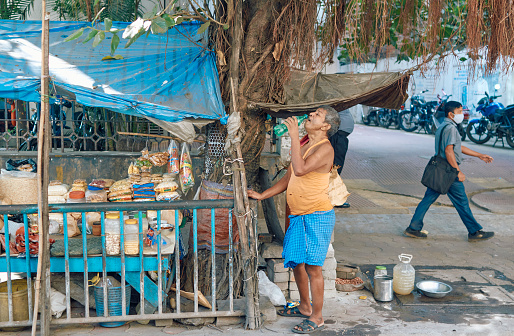 Brabourne Road, Kolkata, 11-16-2020: A simple looking owner of a roadside shop selling puffed rice, snack mix, roasted nuts etc. are drinking water to quench thirst in a hot and humid day.
