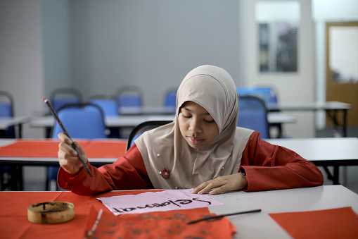 A Muslim girl is practicing to write Selamat Hari Raya (Eid-Ul-Fitr) in Chinese calligraphy style.