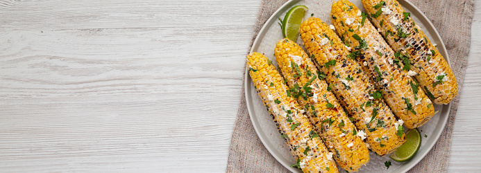 Homemade Elote Mexican Street Corn on a plate on a white wooden background, top view. Flat lay, overhead, from above. Space for text.