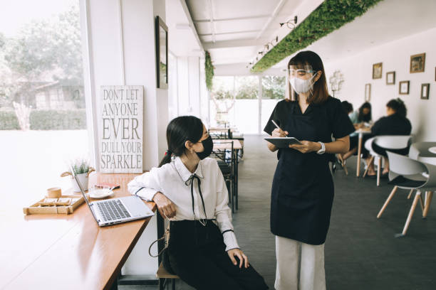 istock Asian beautiful waitress taking client's order, using a digital tablet in a coffee shop- stock photo 1313084013