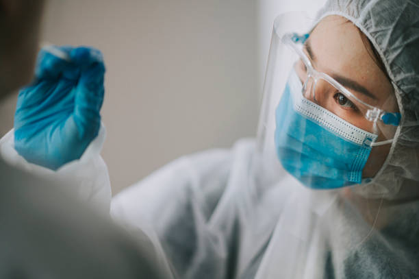 asian chinese female doctor with ppe taking nasal swab from patient coronavirus test. medical worker in protective suite taking a swab for corona virus test, potentially infected woman - protective suit fotos imagens e fotografias de stock