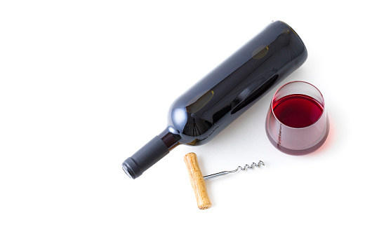 Top view of a drinking glass full of wine beside a red wine bottle and a wooden handle screw cap laying on white background. Studio shot taken with Canon EOS 6D Mark II and Canon EF 100 mm f/ 2.8