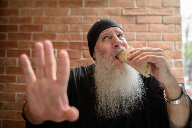 istock Hungry man with long gray beard eating taco while getting disturbed and showing stop gesture 1313092643