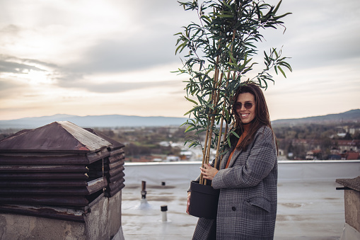 Beautiful young woman with sunglasses carrying potted bamboo plant on rooftop