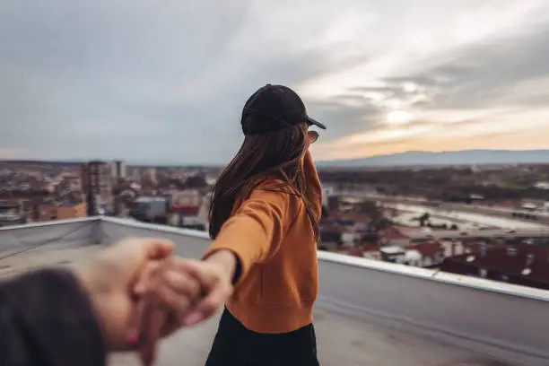 Follow me concept, beautiful young woman standing on rooftop and holding boyfriends hand