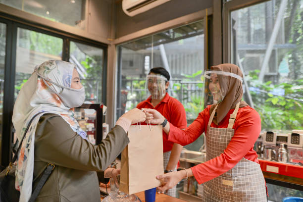 Small business owners serving a customer wearing face mask in the cafe Young cafe owners entrepreneur busy attending pregnant Muslim woman customer small business malaysia stock pictures, royalty-free photos & images