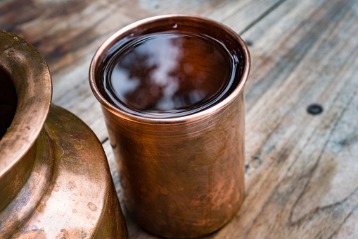 Un soporte de agua de cobre y un vaso. En la cultura ayurvédica india se ha establecido que beber agua de un utensilio de cobre tiene muchos beneficios para la salud. photo
