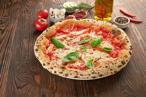 Original italian Pizza Margherita with cheese and tomato sauce on an wooden table with ingredients
