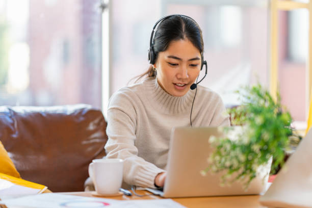 junge frau mit laptop im wohnzimmer zu hause - working at home headset telecommuting computer stock-fotos und bilder