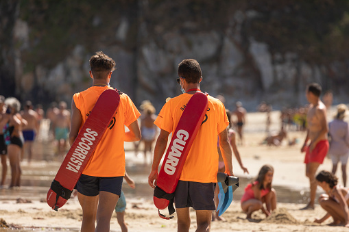 San Pedro de la Ribera, Spain - August 16, 2020: A couple of lifeguards from the public security services walk with the protective face mask on a beach in Asturias, in the middle of summer.