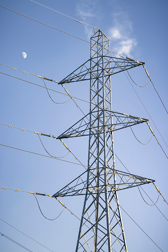 Electricity pylon with the moon against a blue sky, depicting UK National Grid and electricity power supply