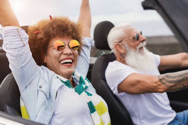 Trendy senior couple having fun inside convertible car - Multiracial mature people on a road trip with cabriolet car Trendy senior couple having fun inside convertible car - Multiracial mature people on a road trip with cabriolet car convertible stock pictures, royalty-free photos & images