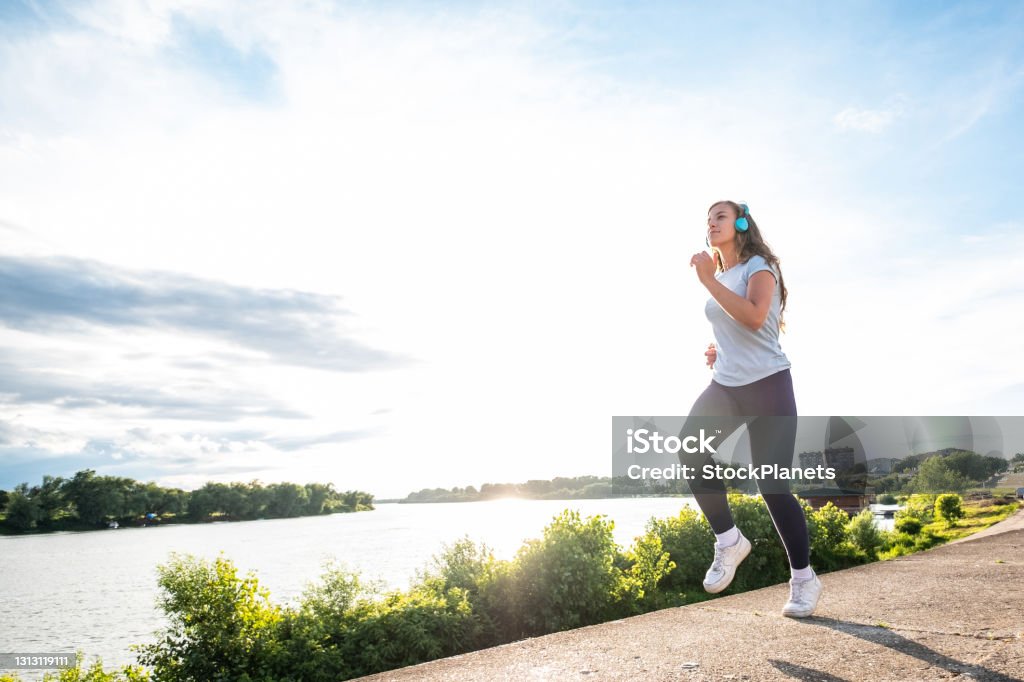 Teenager girl exercise at the riverbank Teenager girl jogging and listen to music at the riverbank Jogging Stock Photo