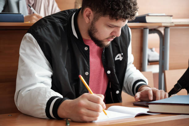 istock Serious guy in casualwear bending over desk and making notes in copybook while using smartphone 1313119458