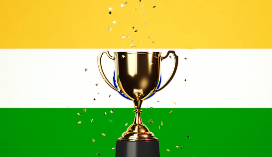 Star shaped gold confetti falling onto a gold cup sitting over Indian flag background. Horizontal composition with copy space. Front view. Championship concept.