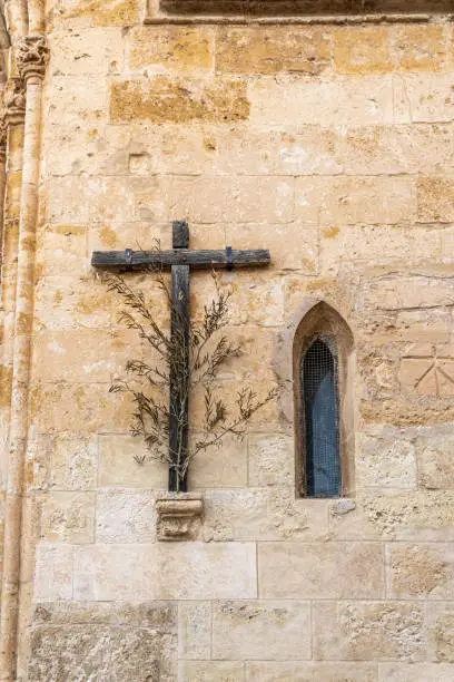Photo of Wooden cross with olive branch next to a Gothic window on the main facade of the Christian church of Sineu