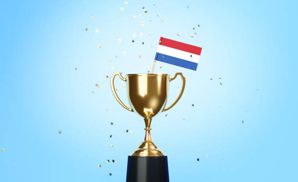 istock Championship Concept - Star Shaped Confetti Falling Onto A Gold Cup In Which Tiny Dutch Flag Sitting Before Blue Background 1313123486