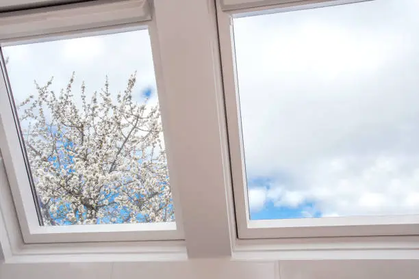 Photo of A modern open skylight,mansard window against blue sky with beautiful tree with white flowers, modern new house design, architectural detail