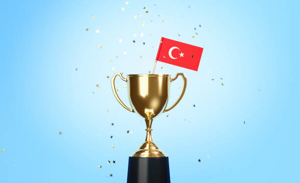 istock Championship Concept - Star Shaped Confetti Falling Onto A Gold Cup In Which Tiny Turkish Flag Sitting Before Blue Background 1313124789
