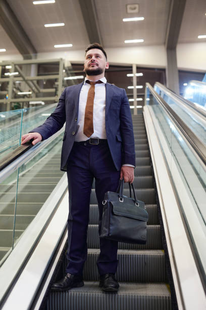 istock Contemporary middle aged businessman holding black leather handbag while standing on escalator 1313124960