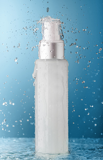 Cosmetic bottle with falling water and splashes on blue background. Concept of fresh and beauty.