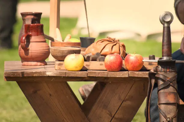 A soldiers lunch set out on a bench during a historical reenactment day, with sword hilt, apples and some terracotta bowls