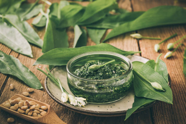 pesto de alho selvagem caseiro em uma tigela de vidro no fundo de madeira, decorado com folhas e pinheiros, cores dessasaturadas - ramson - fotografias e filmes do acervo