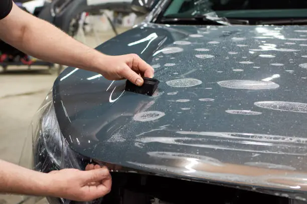 Photo of Installation of a protective paint and varnish transparent film on the car. PPF polyurethane film to protect the car paint from stones and scratches.