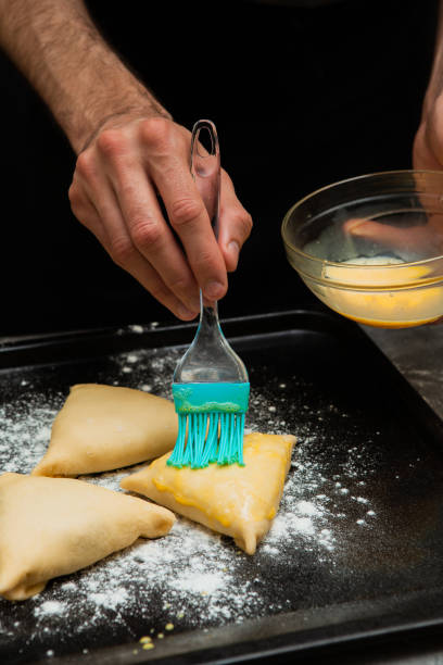 istock a male cook greases triangular pies with cabbage with a brush with an egg. hands close up. food on the pan. 1313135763