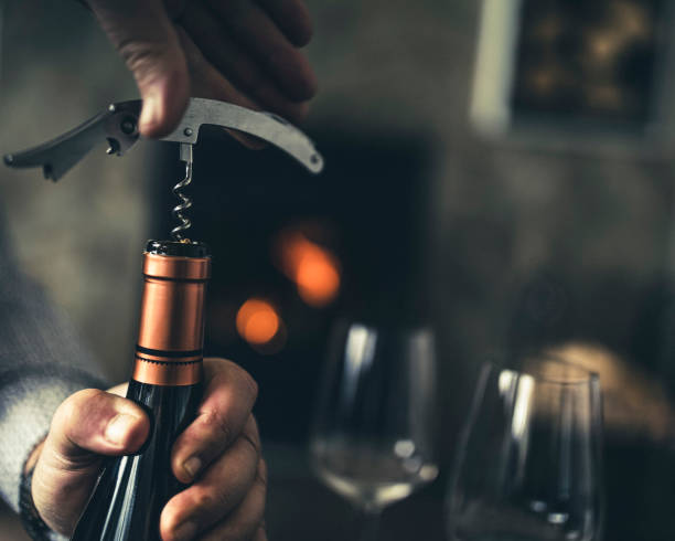 Close-up of a man, with a corkscrew in his hand, opening a bottle of white wine. stock photo