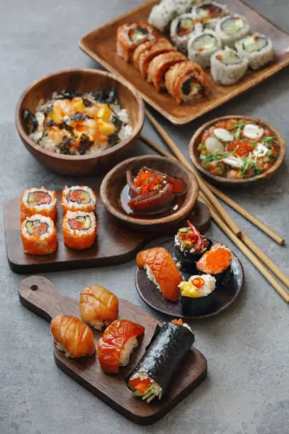 Sushi and sushi roll set (Sake nigiri sushi, notate nigiri sushi, Philadelphia rolls, spicy tuna roll, scallop roll). Tuna tataki. Raw scallop rice bowl with mango, spicy mayo, tobiko caviar and nori chips. Gunkan set. Temaki. Close-up composition on concrete background.