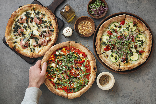 Man eating Italian Pizza with Mortadella. Pizza with zucchini and sun-dried tomatoes. Pizza with vegetables. Flat lay top-down composition on concrete background.